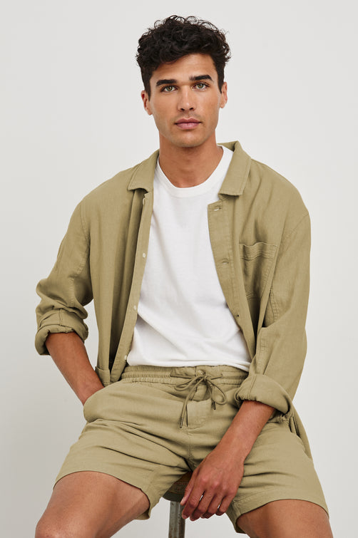 Archer long length cotton short with adjustable drawstring and front button closure in True Khaki - front view on model, sitting on chair