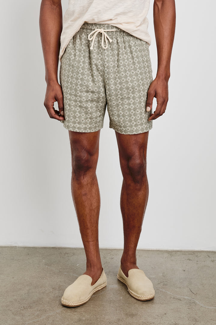 Aries mid length linen short in Diamond Oat Olive art deco pattern - front view, lower half of model