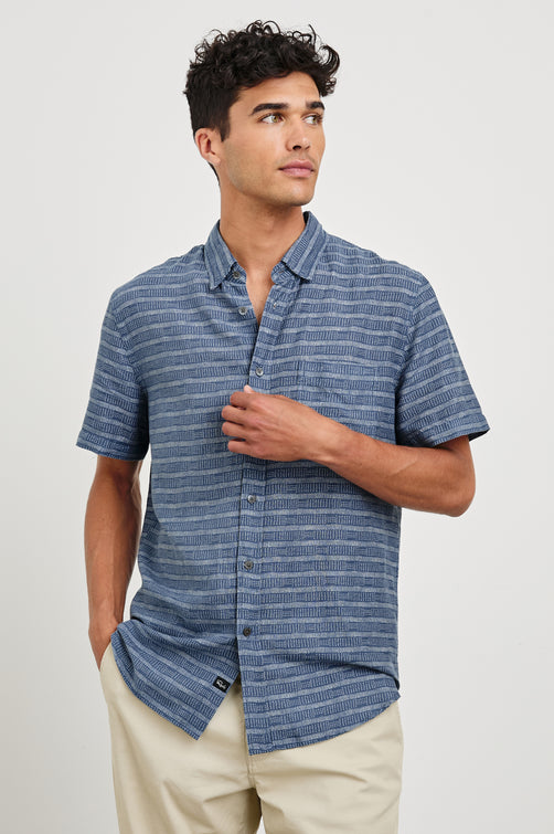 Carson linen short sleeve button down with a collar and blue textured stripe pattern in Homespun Border Blue - front view on model, hand on buttons