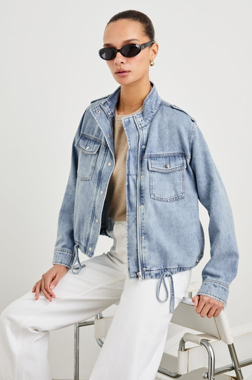 Collins military style jacket with cargo chest pockets and drawstring hem in Faded Indigo - front view on model sitting with sunglasses