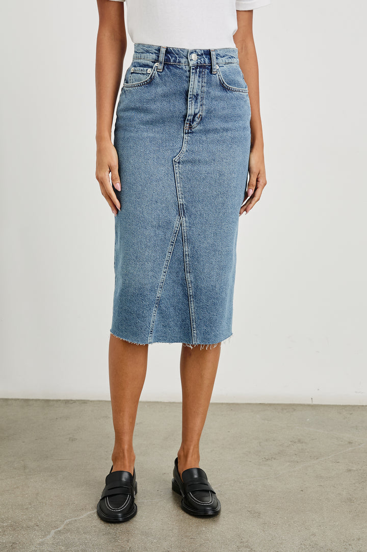 Highland Denim Midi Skirt with a Raw Hem, a Back Vent, Additional Front Seams, Belt Loops, Two Front Pockets plus a Coin Pocket and Two Back Patch Pockets in Vintage Sapphire Colorway - Front View Featured on Model 