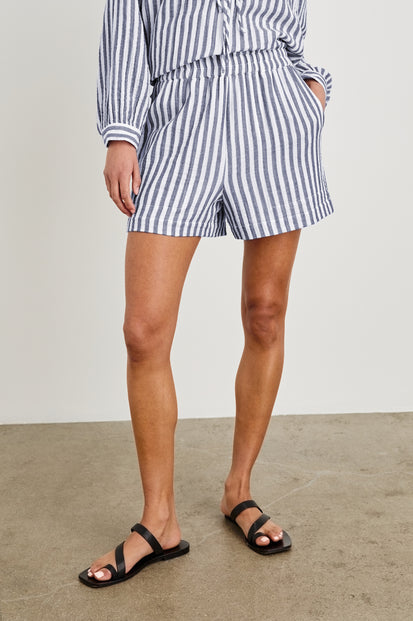 Model is wearing our Leighton Short featuring blue and white vertical stripes. High rise, lined, with a smocked elastic waistband. Styled with matching Brielle Top. 