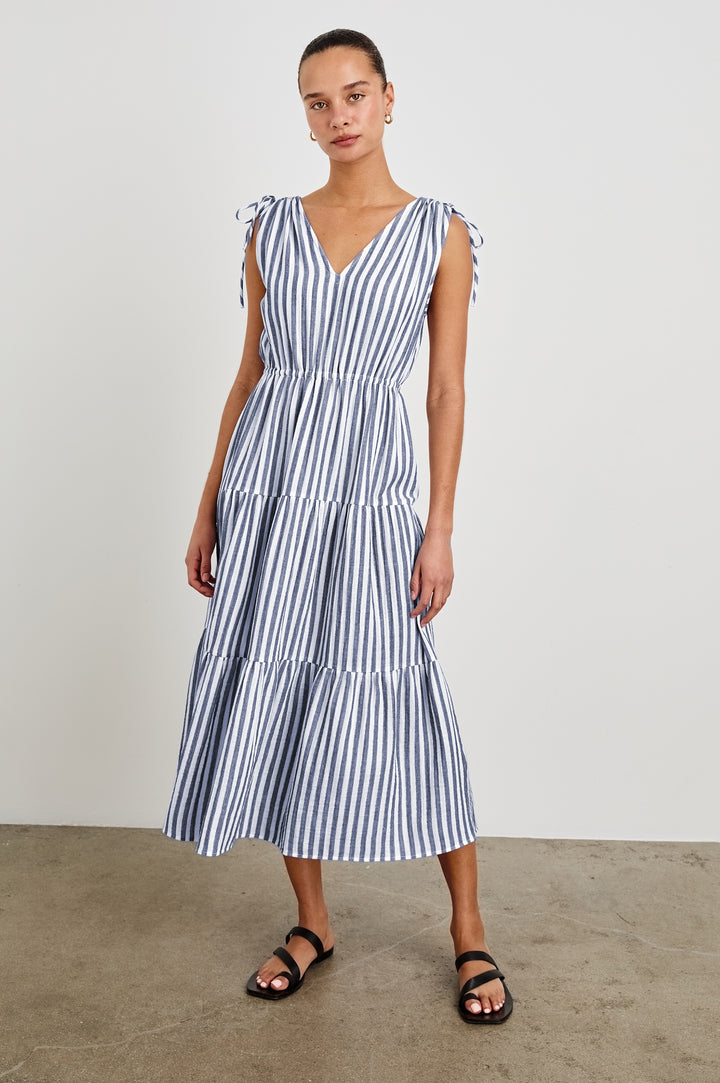 Model is wearing a tiered midi dress featuring blue and white vertical stripes. Suzette dress features an elasticated waist and customizable shoulder straps.