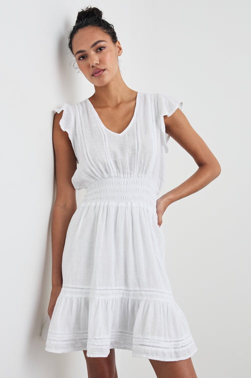 Tara Short Sleeve, Above the Knee Dress with a Smocked Waist, V Neck, Flutter Cap Sleeves, and Tiered Skirt with a Ruffled Hem in White Lace Detail Colorway, with Vertical Lace Inserts on the Bodice and Horizontal Inserts on the Skirt - Front View Featured on Model 