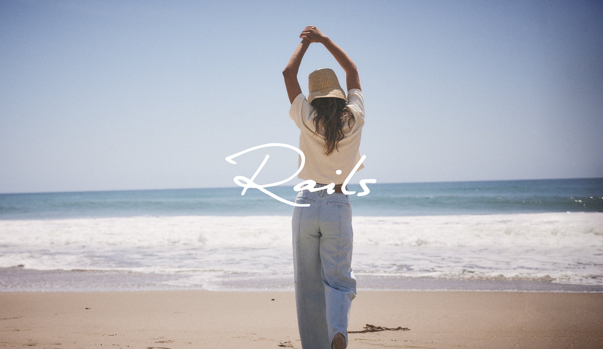 BACK FULL BODY EDITORIAL IMAGE OF MODEL STANDING ON THE BEACH WEARING GETTY CROP UTILITY JEANS IN OCEANVIEW